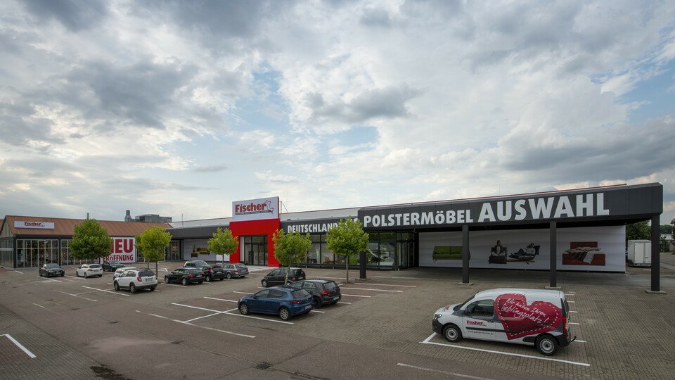 Großer Möbelmarkt mit Parkplatz und Fahrzeugen.