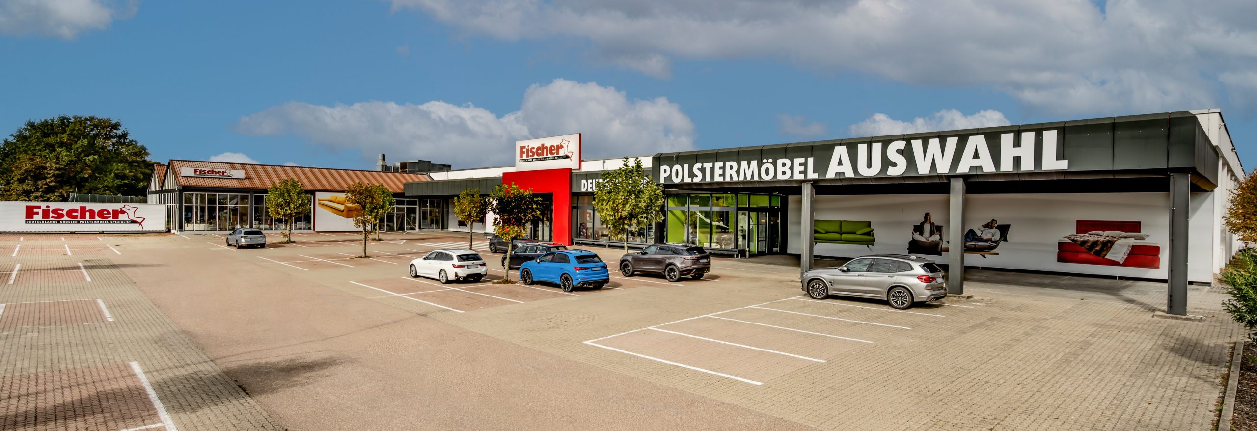 Polstermöbel Fischer Filiale in Bruchsal mit moderner Glasfassade, rotem Eingang und großer Aufschrift ‚Polstermöbel Auswahl‘ – Außenansicht mit Kundenparkplatz.