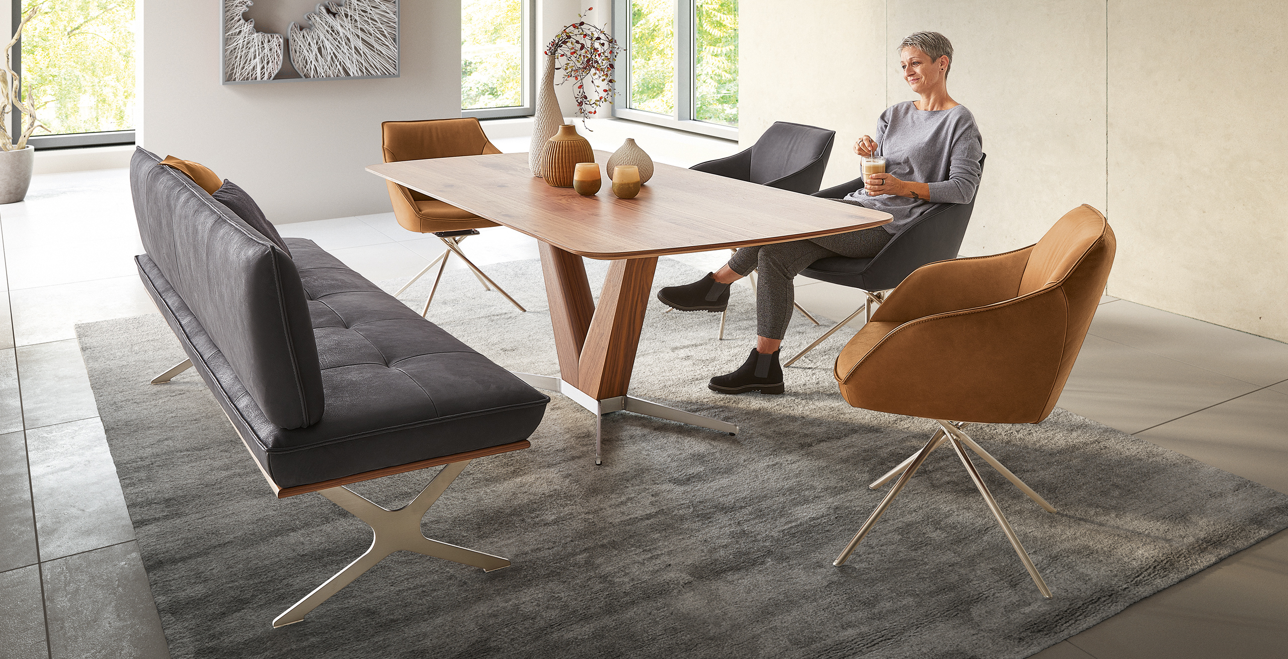 Modernes Koinor Dining Set mit schwarzer Lederbank, braunen Drehstühlen und einem Esstisch mit Holzplatte – stilvolle Essgruppe auf grauem Teppich im lichtdurchfluteten Raum.
