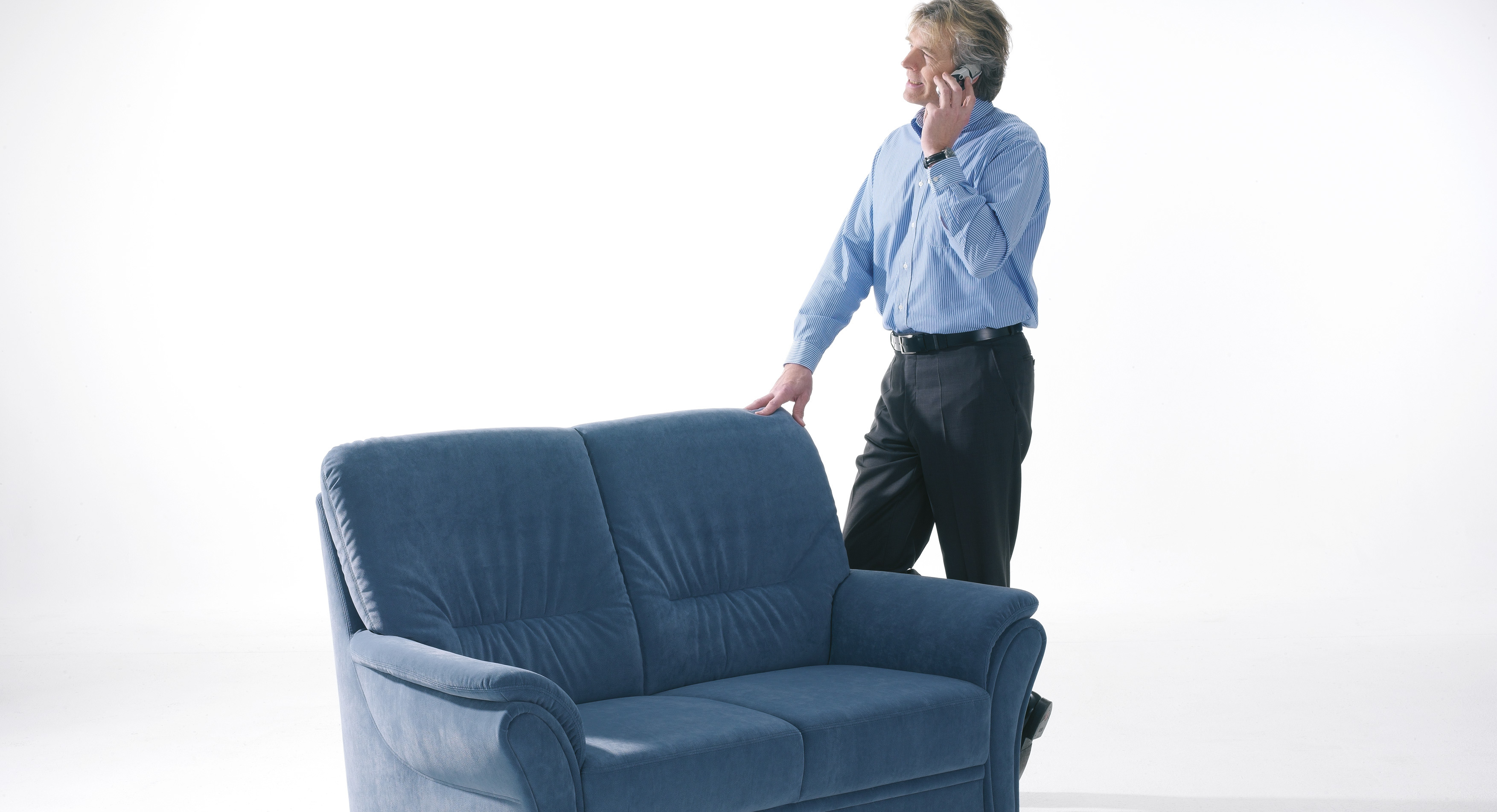 Mann telefoniert neben blauer Couch.