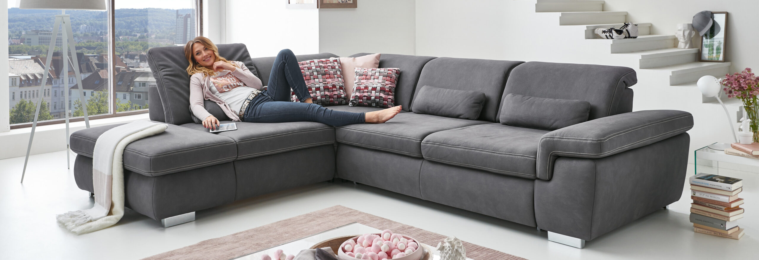 Frau entspannt auf gemütlichem Ecksofa mit Stadtpanorama.