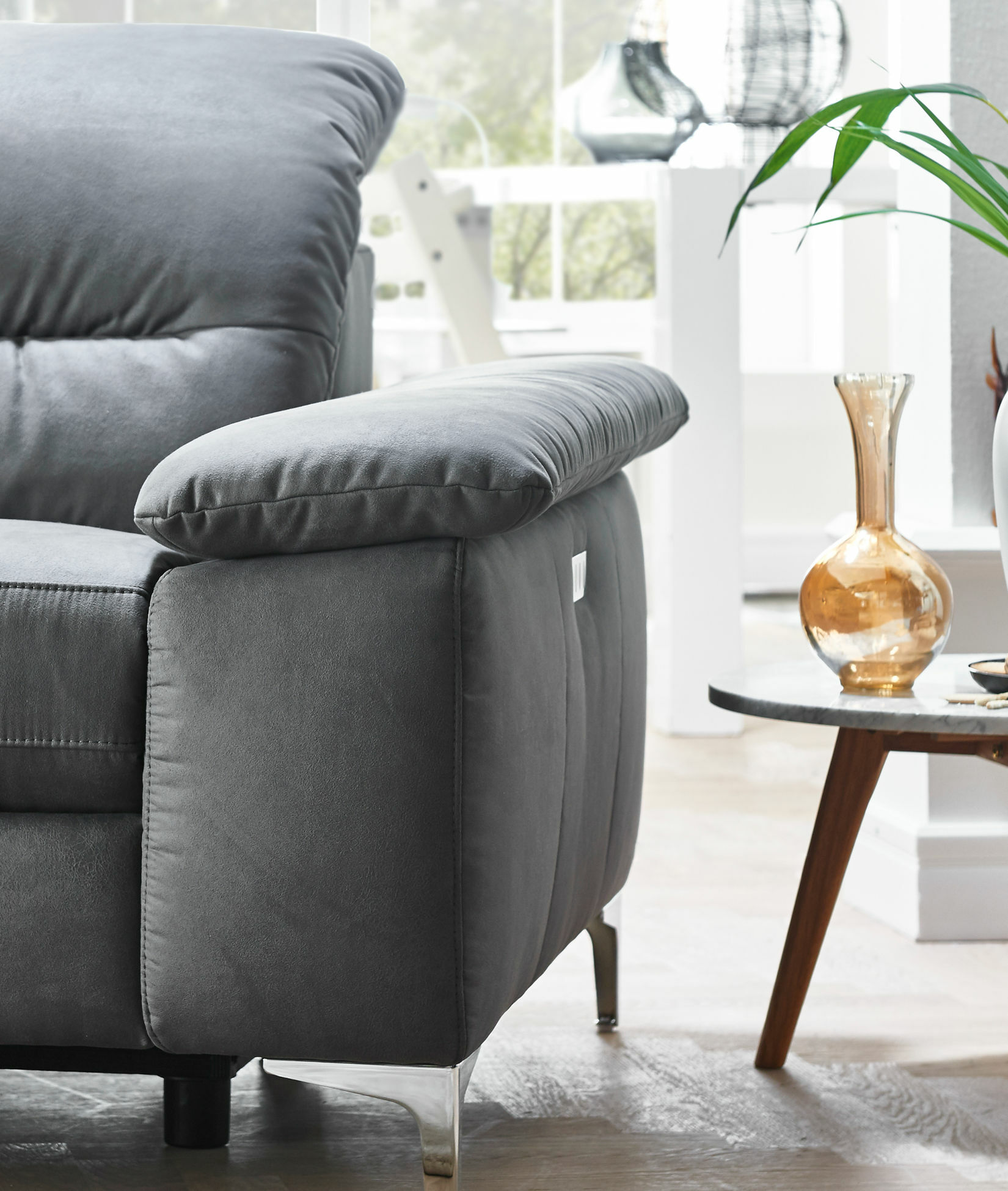 Graues Sofa mit grüner Pflanze und Vase.