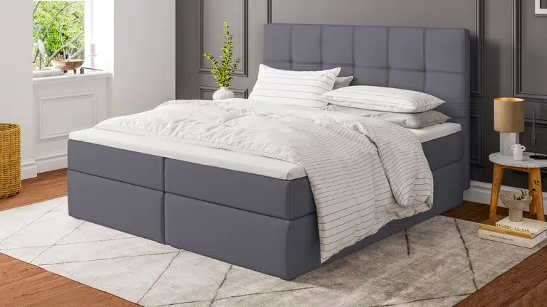 Modernes Schlafzimmer mit grauem Boxspringbett.