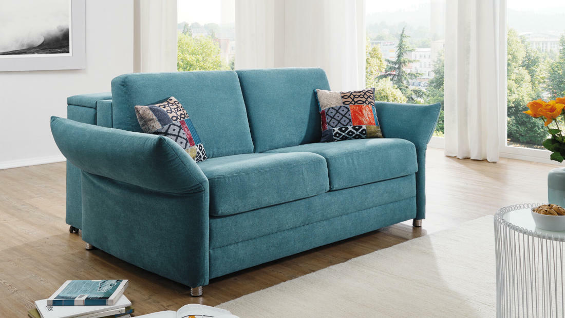 Komfortables teal-farbenes Sofa mit gemusterten Kissen.