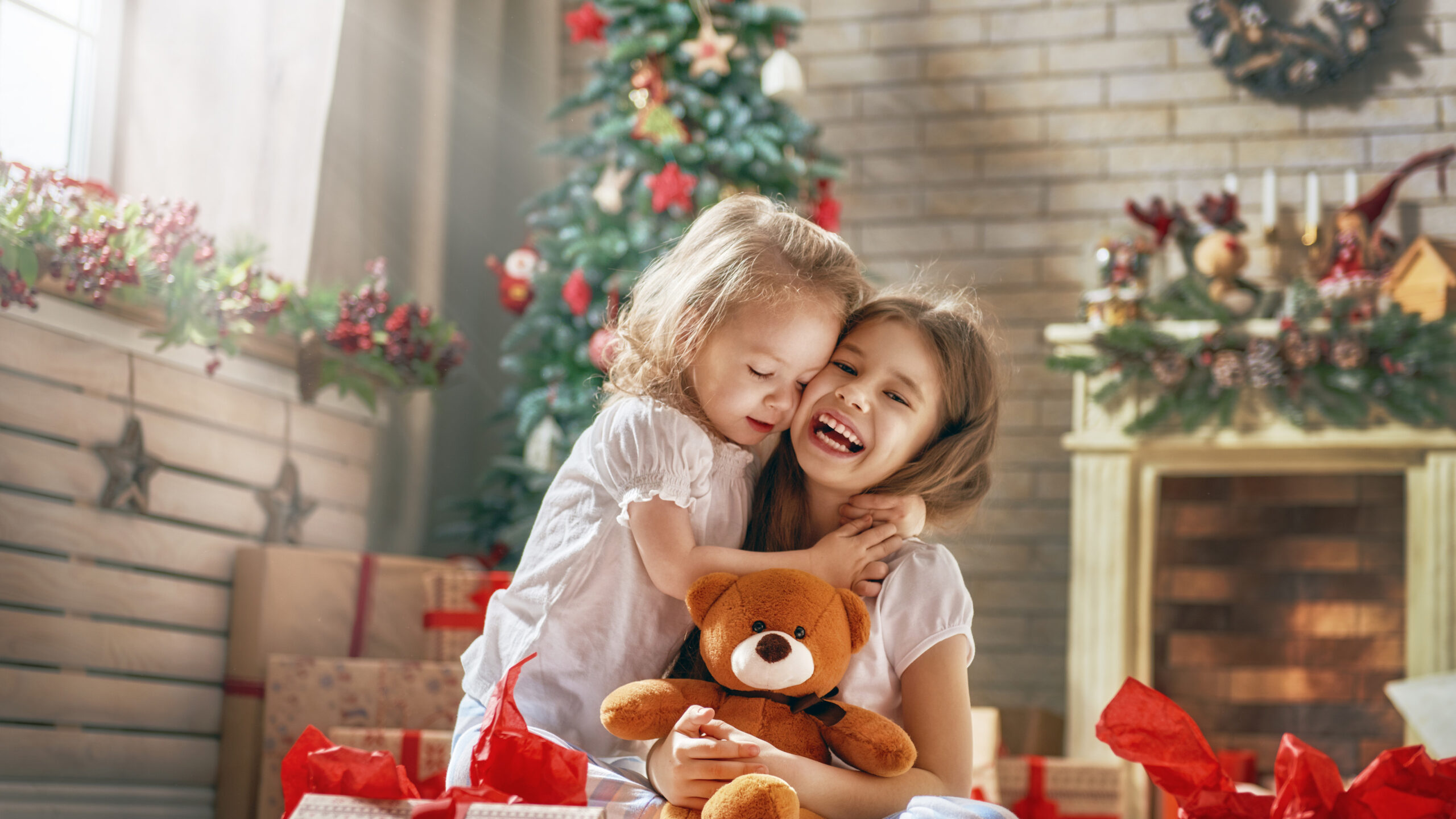 Zwei Mädchen umarmen sich fröhlich vor Weihnachtsdekorationen.