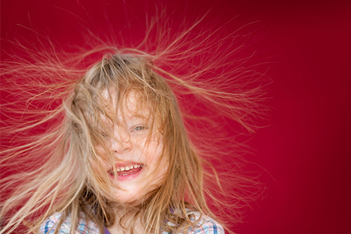 Windverwehtes blondes Haar vor rotem Hintergrund.