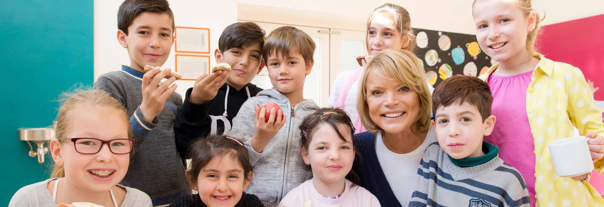 Gruppe glücklicher Kinder und Lehrer in buntem Klassenzimmer.