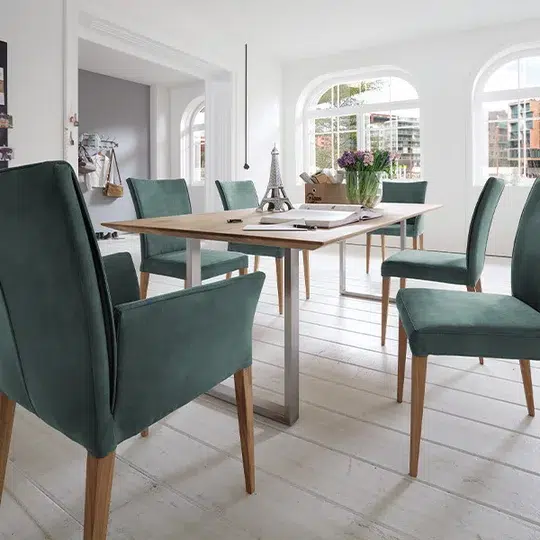 Helles, geräumiges Esszimmer mit Holztisch und grünen Stühlen.