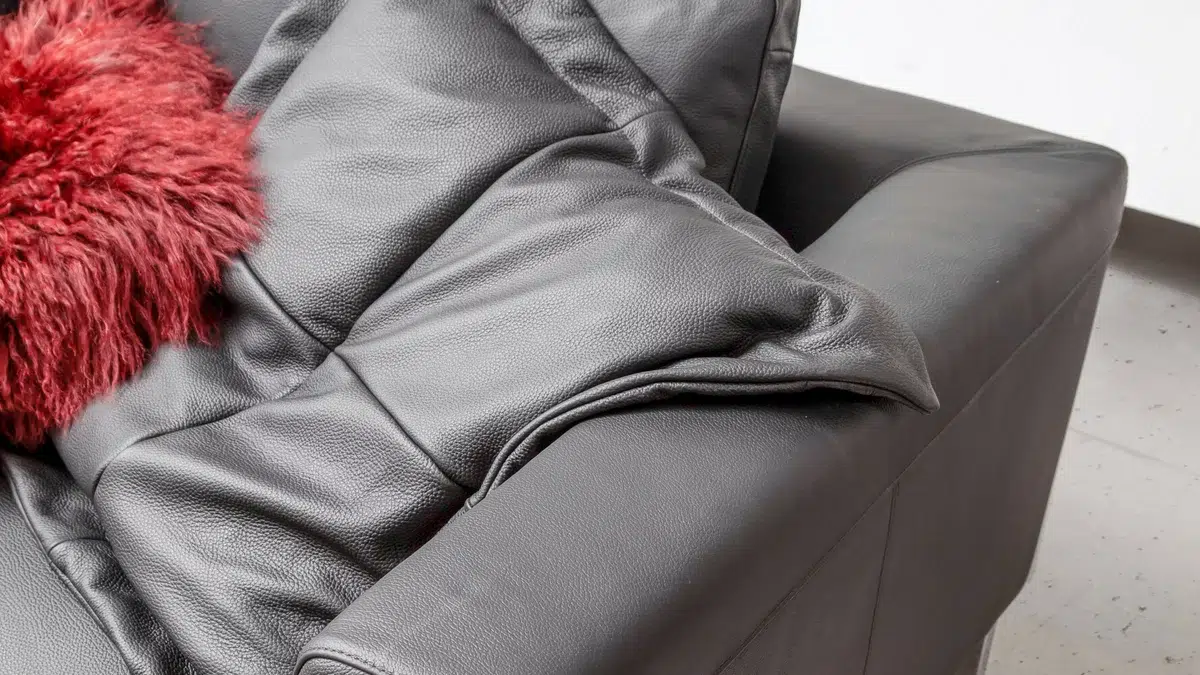 Graue Ledercouch mit rotem Kissen.