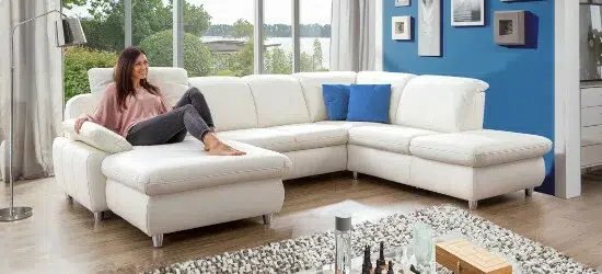 Eine Frau sitzt auf einem weißen Ecksofa in einem Wohnzimmer.