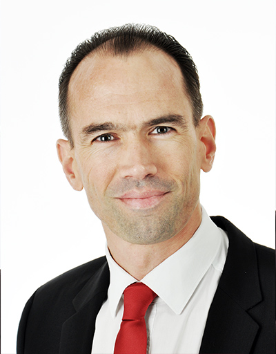 Businessman in black suit, red tie, and confident expression.