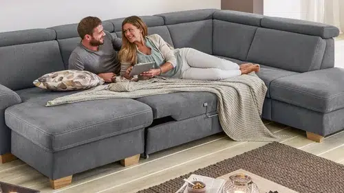 Paar entspannt auf grauer Couch mit Snacks.