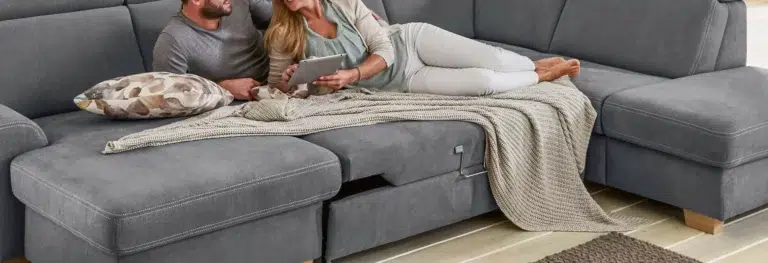 Paar entspannt auf grauem Sofa mit Tablet.