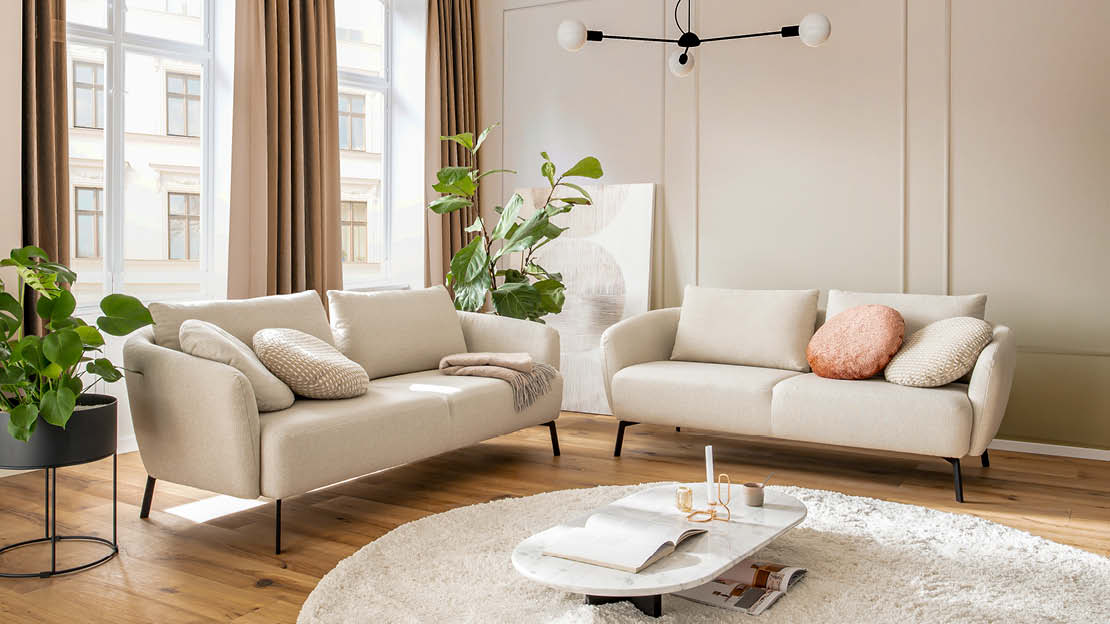 Gemütliches Wohnzimmer mit zwei beigefarbenen Sofas, runden Kissen und Pflanzen im hellen Vanilla-Girl-Ambiente.