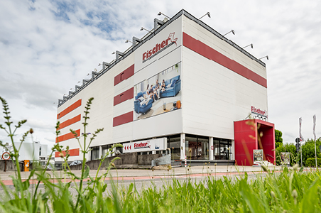Polstermöbel Fischer Filiale in Fellbach mit großem Fassadenbild einer Wohnlandschaft – auffälliges weißes Gebäude mit roten Streifen und rotem Eingangsbereich.