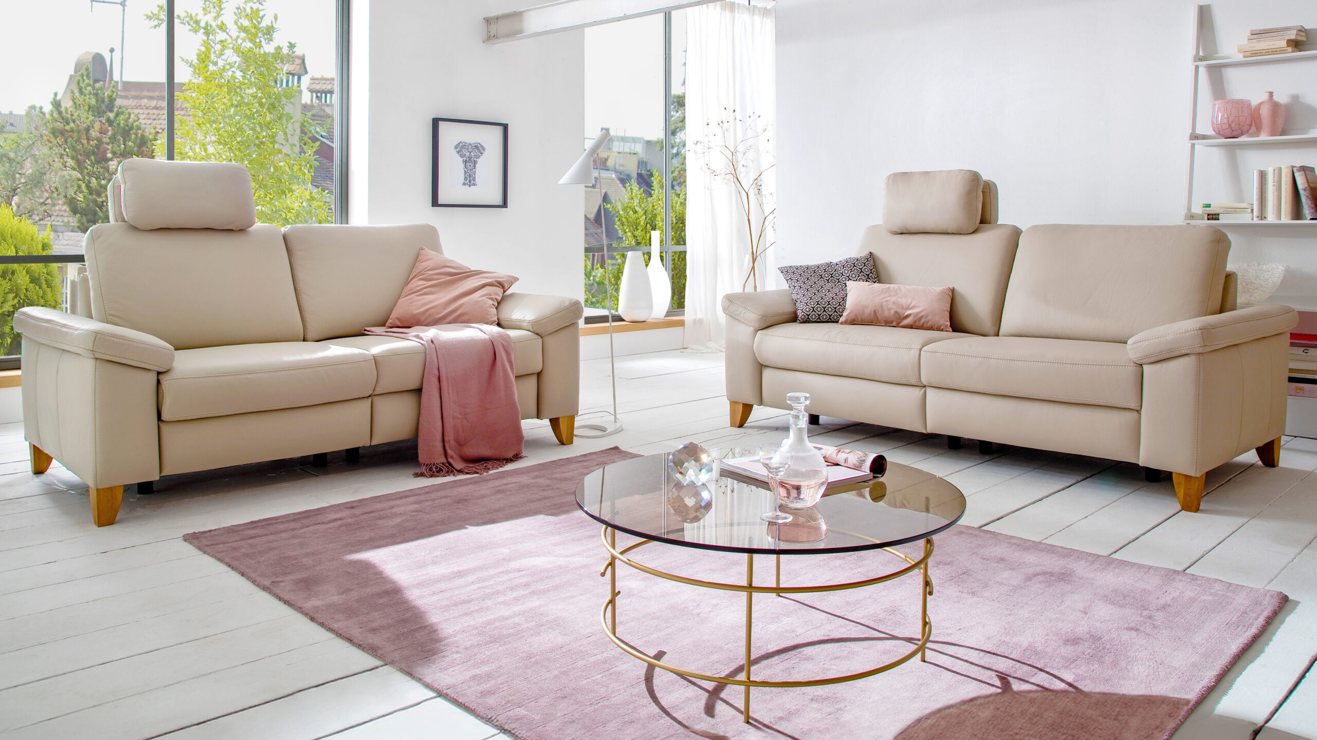 wei klassische Einzelsofas aus beigefarbenem Leder mit Holzfüßen, dekoriert mit Kissen und Decke in einem hellen Wohnzimmer mit rosa Akzenten.