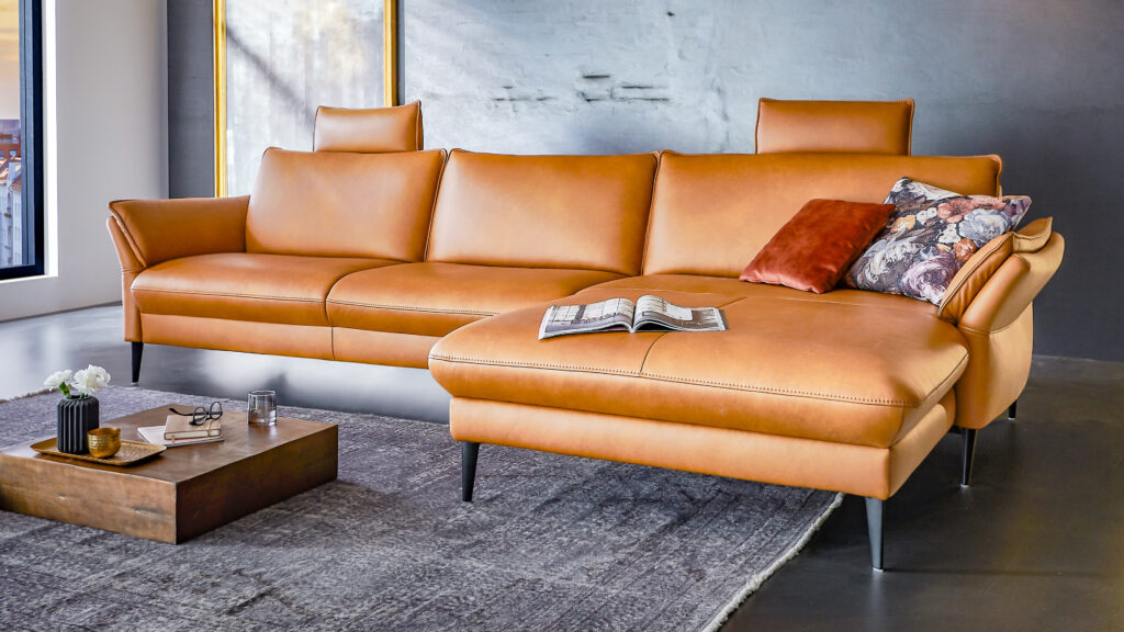 Elegantes Ledersofa in Cognac mit hoher Rückenlehne, modernen schwarzen Füßen und dekorativen Kissen in einem stilvollen Ambiente.