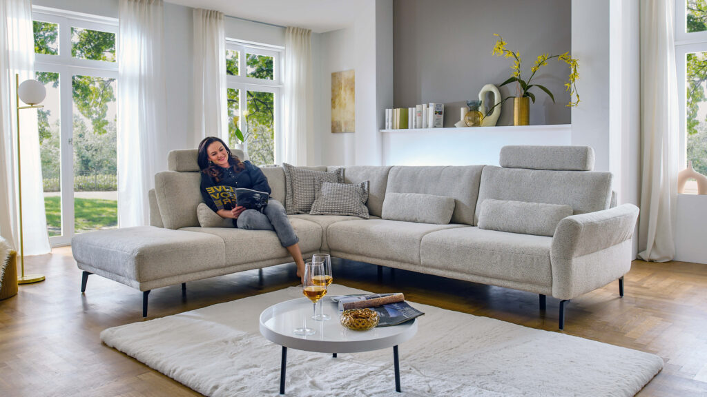 Frau entspannt auf dem Ecksofa EO121 mit Kopflehne – Wohlfühlmoment auf stilvollem Bouclé-Sofa.