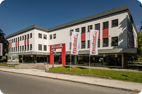 Polstermöbel-Fischer-Filiale in Bad Reichenhall mit roten Fassadenelementen, markantem Eingang und mehreren Hissflaggen entlang der Straße.