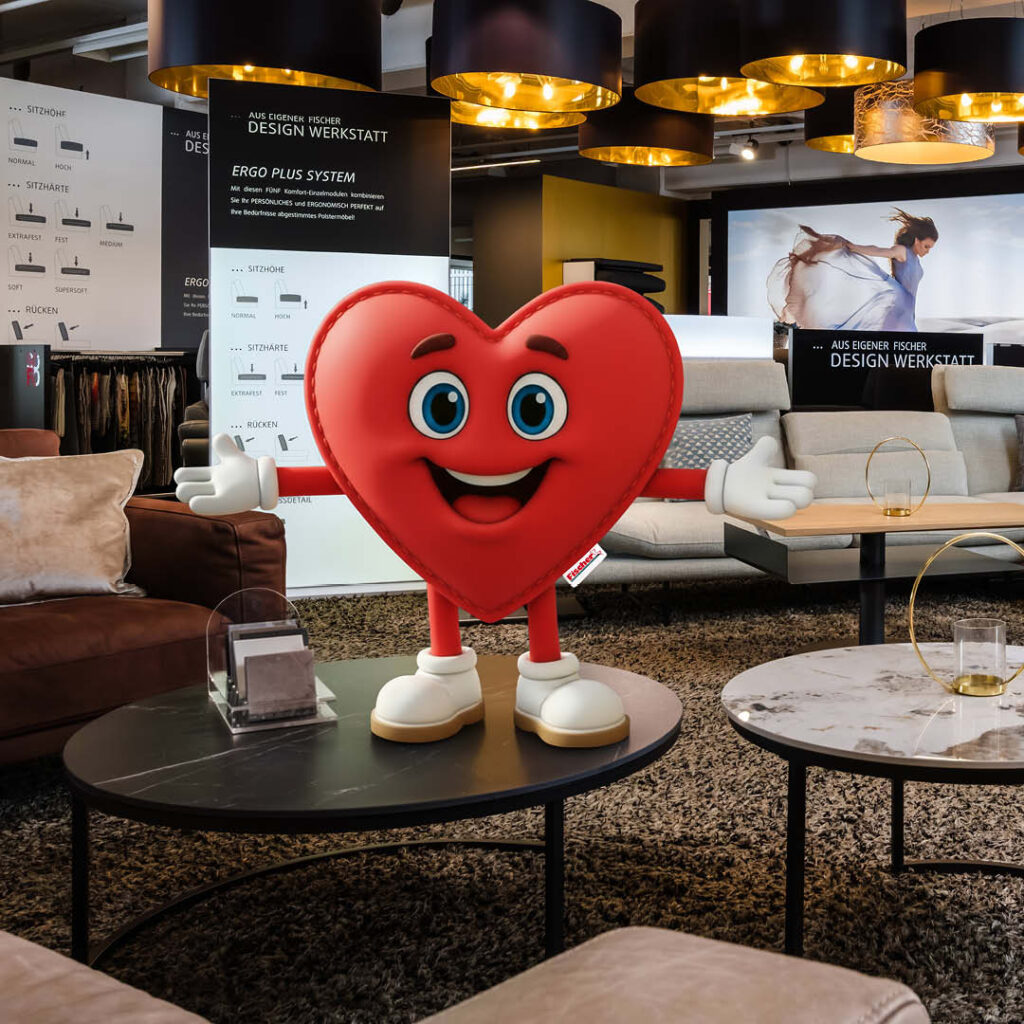 Rotes Herz-Maskottchen von Polstermöbel Fischer begrüßt Kunden in der Design Werkstatt – individuelle Sofa-Beratung