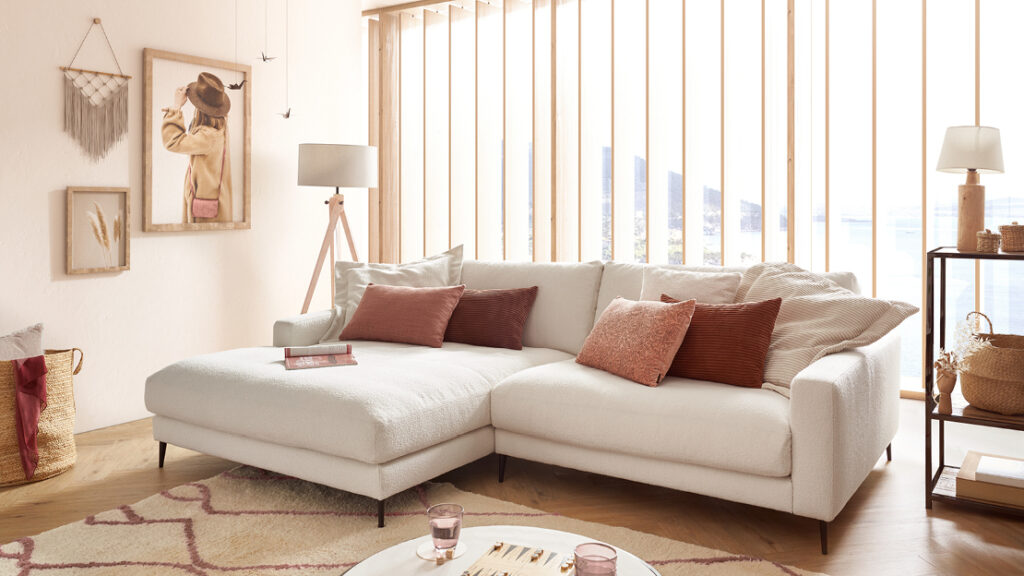 Helles Wohnzimmer mit weißem Sofa, roten Kissen und warmen Holzelementen – stilvolle Boho-Einrichtungsidee von Polstermöbel Fischer.
