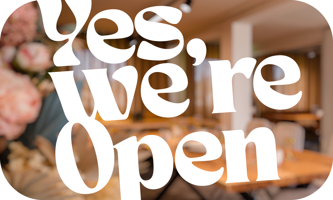 Grafik mit dem Schriftzug „Yes, we’re open“ vor einem unscharf dargestellten, warm eingerichteten Innenraum – Hinweis auf geöffneten Verkaufstag bei Polstermöbel Fischer.