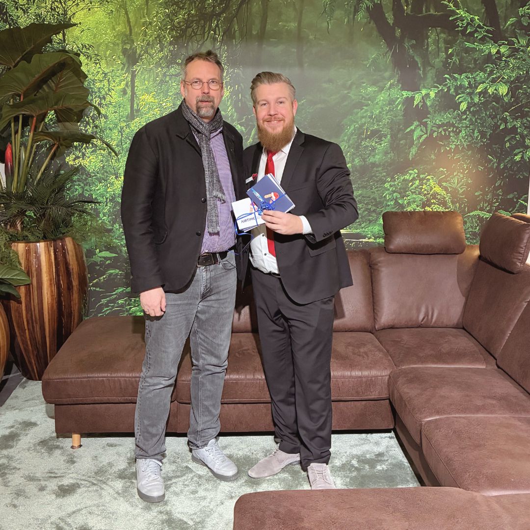 Spenden&uuml;bergabe von Polsterm&ouml;bel Fischer an das Martin-Luther-Haus: zwei M&auml;nner im Showroom vor brauner Wohnlandschaft mit Kopfst&uuml;tzen