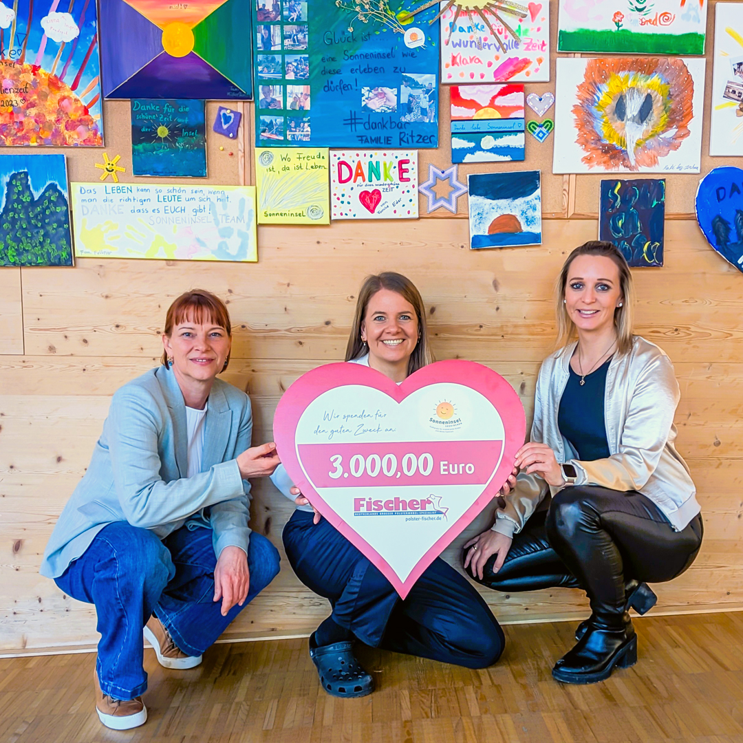 drei frauen kniend vor wand mit gemalten kinderbildern bei &uuml;berg&auml;be eines spendenschecks an die sonneninsel seekirchen