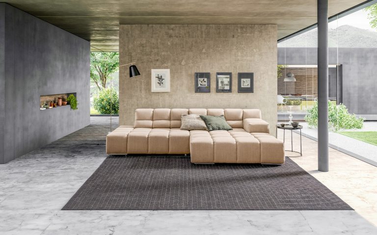 Beiges Wohnlandschaft-Sofa in modernem Architekturhaus mit Betonoptik, Teppich und großer Glasfront