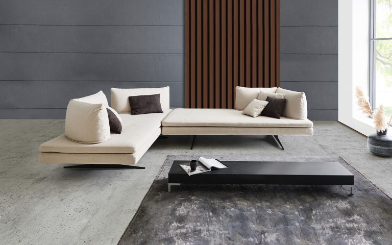 Modernes Loungesofa in Creme mit niedriger Sitzfläche und Kissen vor dunkler Designwand