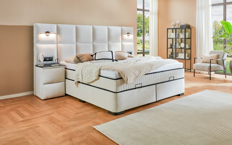 Helles Boxspringbett mit großem gepolstertem Kopfteil in modernem Schlafzimmer mit warmen Naturtönen